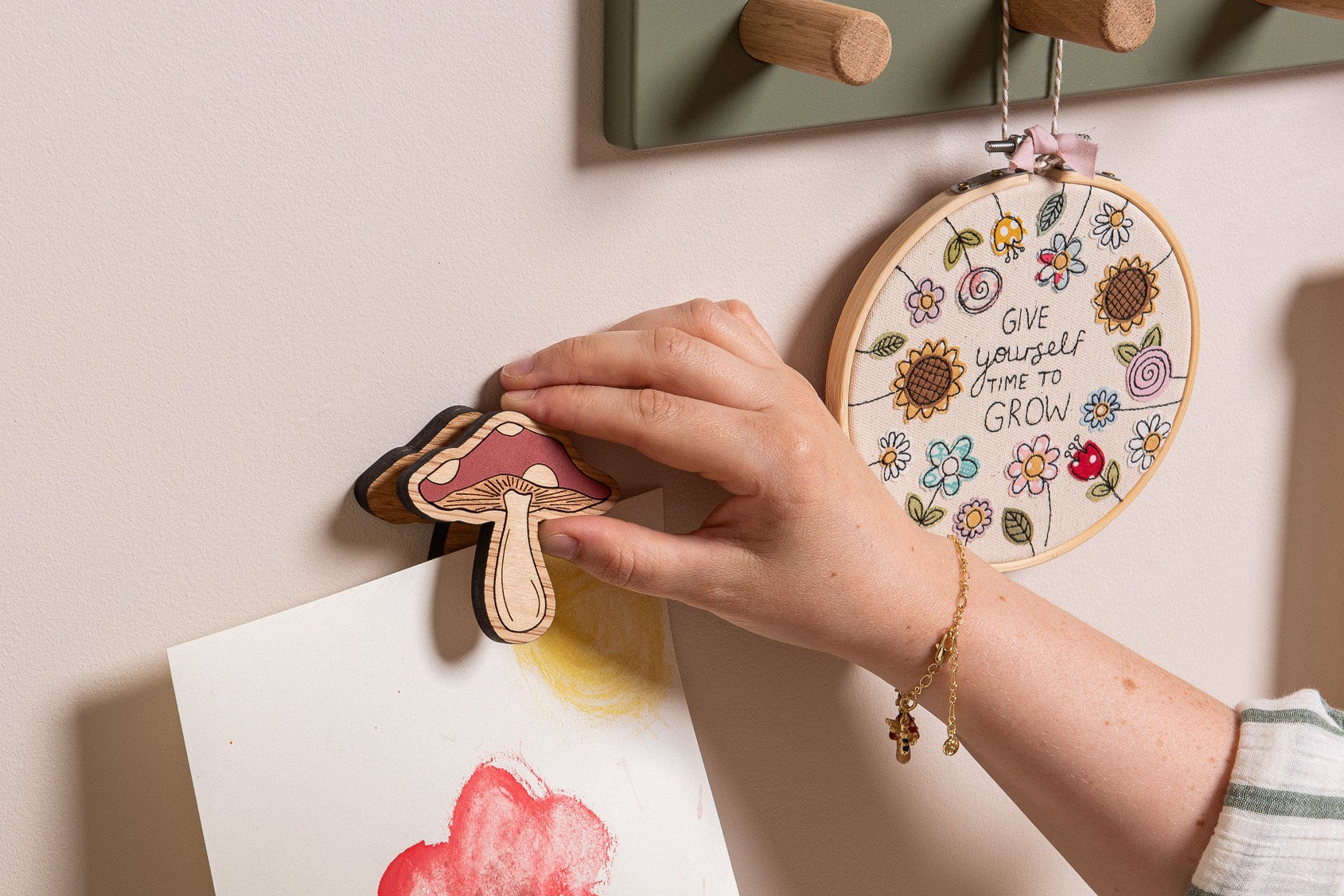 Hand hanging a decorative mushroom on a wall with other art pieces.