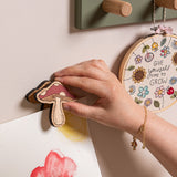 Hand hanging a decorative mushroom on a wall with other art pieces.