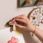 Hand hanging a decorative mushroom on a wall with other art pieces.