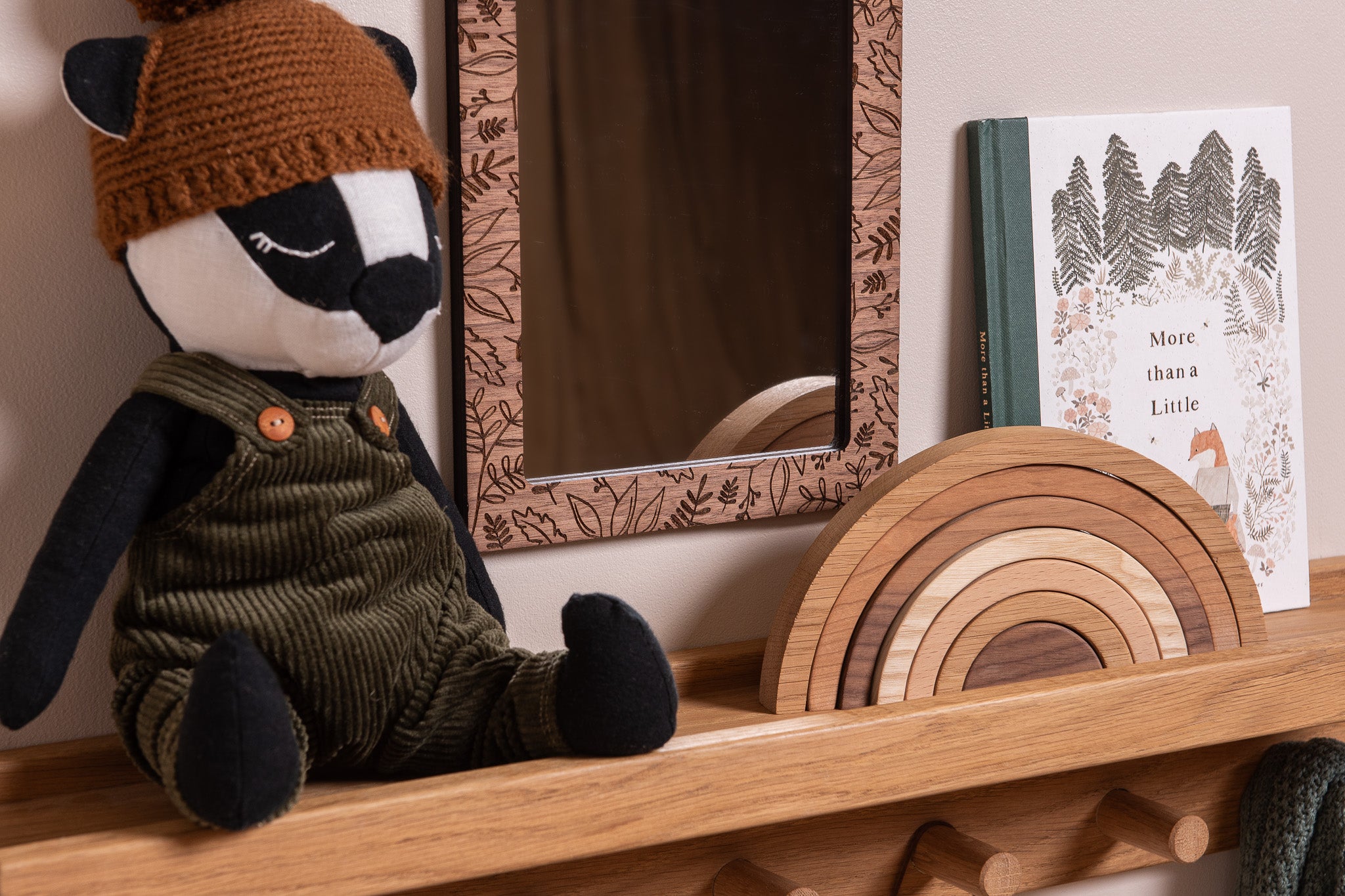 Stuffed animal in a hat and overalls on a wooden shelf with a mirror and book in the background.
